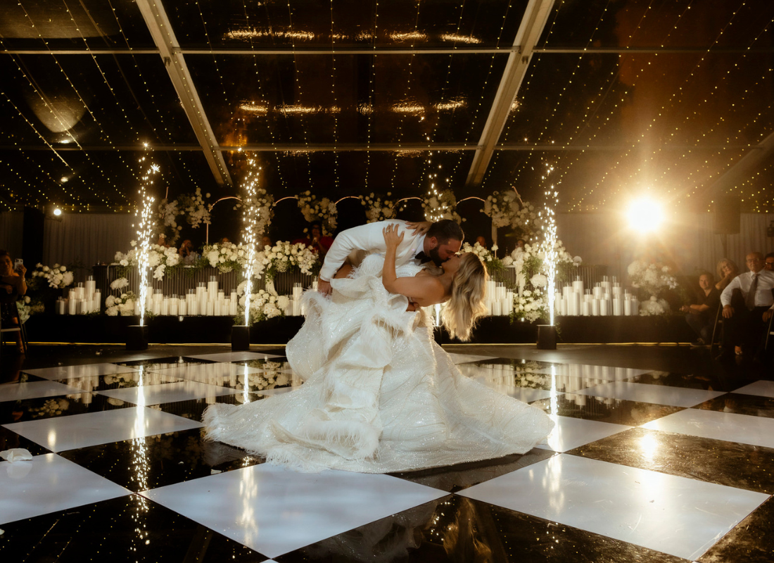 Bride and Groom on checkered dancefloor under fairy lights and abundance of greenery and candlelight